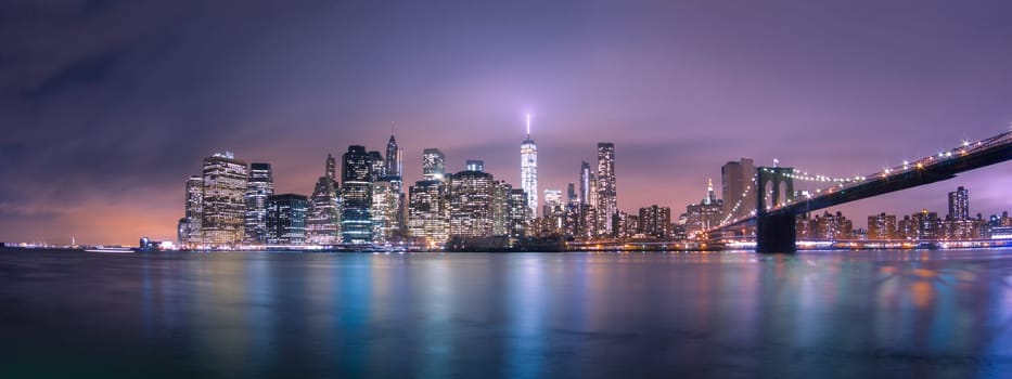 Manhattan bridge and New York City downtown skyline at dusk with skyscrapers illuminated over East River panorama. Copy space.