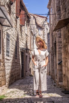 Beautiful blonde young female traveler wearing straw sun hat sightseeing and enjoying summer vacation in an old traditional costal town at Adriatic cost, Croatia