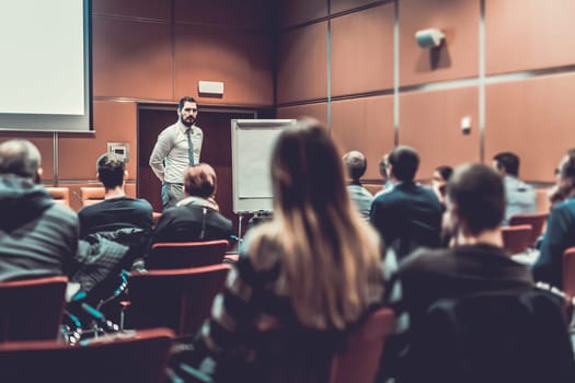 Public Speaker Giving a Talk at Business Meeting. Audience in the conference hall. Skilled coach answers questions of participants of business training. Business and Entrepreneurship concept.