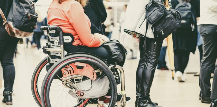 Close up of unrecognizable hanicapped woman on a wheelchair waiting in line to perform everyday tasks.