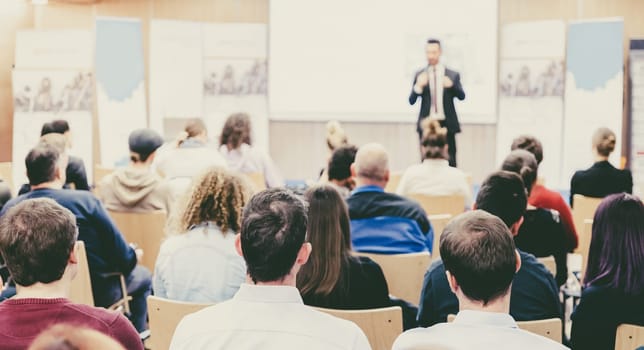 Speaker giving a talk in conference hall at business event. Audience at the conference hall. Business and Entrepreneurship concept. Focus on unrecognizable people in audience.