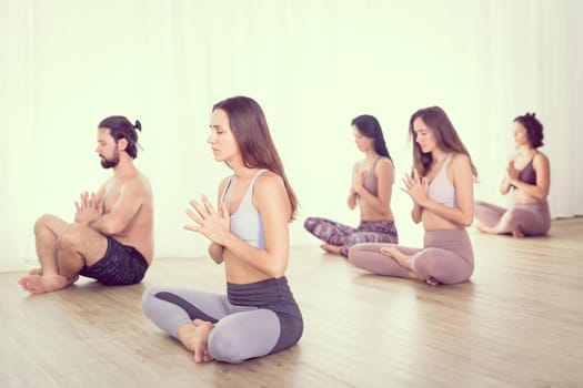 Group of young sporty attractive women in yoga studio, practicing yoga lesson with instructor, stretching and relaxing during workout . Healthy active lifestyle, working out in gym