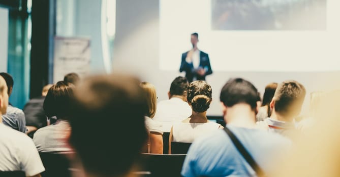 Male speaker giving a talk in conference hall at business event. Audience at the conference hall. Business and Entrepreneurship concept. Focus on unrecognizable people in audience.