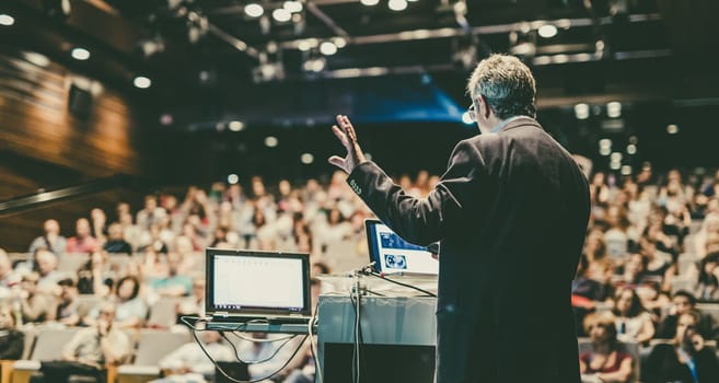 Speaker giving a talk on corporate business conference. Unrecognizable people in audience at conference hall. Business and Entrepreneurship event.