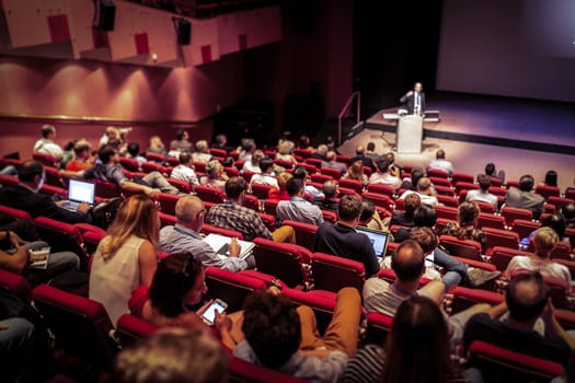 Speaker giving a talk in conference hall at business event. Audience at the conference hall. Business and Entrepreneurship concept. Focus on unrecognizable people in audience.