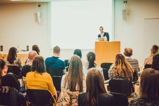Speaker Giving a Talk at Business Meeting. Audience in the conference hall. Business and Entrepreneurship. Focus on unrecognizable people from rear.