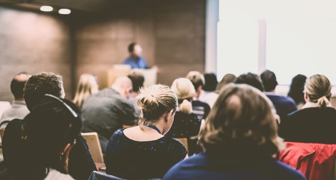 Business and entrepreneurship symposium. Speaker giving a talk at health care workshop meeting. Audience in conference hall. Rear view of unrecognized participant in audience.
