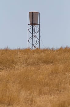 Water tank in the middle of dry pastures. Lack of water resources for cattle concept