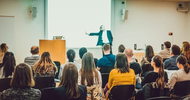 Speaker Giving a Talk at Business Meeting. Audience in the conference hall. Business and Entrepreneurship. Focus on unrecognizable people from rear.