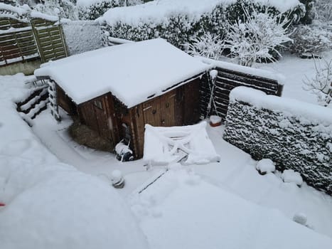 House and garden trees covered in snow on a cold, sunny winters day with clear, blue, azure skies