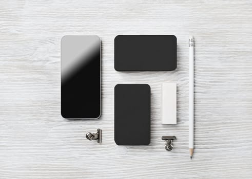 Blank black stationery set and smartphone on light wood table background. Branding mock up. Flat lay.
