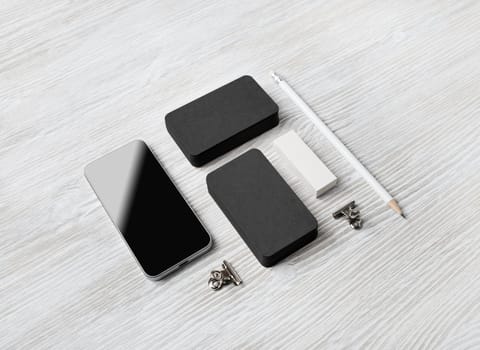 Blank stationery mockup. Blank black business cards, smartphone, pencil and eraser on light wooden background. Brand ID set.