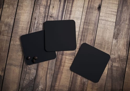 Photo of three blank black square beer coasters and coffee beans on wood table background. Top view. Flat lay.