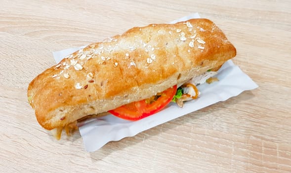 Ciabatta sandwich with lettuce, chicken and cheese on a wooden table.