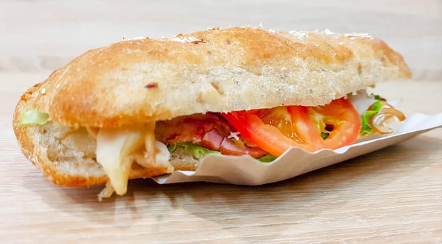 Ciabatta sandwich with lettuce, chicken and cheese on a wooden table.