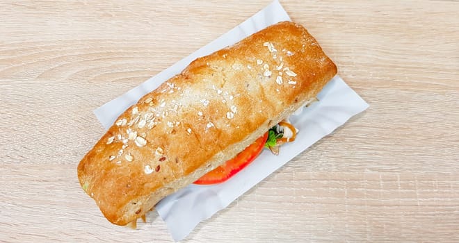 Ciabatta sandwich with lettuce, chicken and cheese on a wooden table.