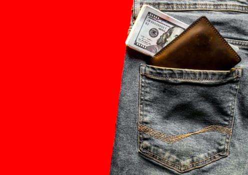 banknotes in your jeans pocket in your wallet. The concept of wealth and wages for work. Wallet and dollars in jeans pocket. Copy space, place for text, flat lay. Blue jeans on a red background.