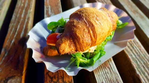 Croissant with avocado, tomato and herbs outdoors. Street vegetarian food.