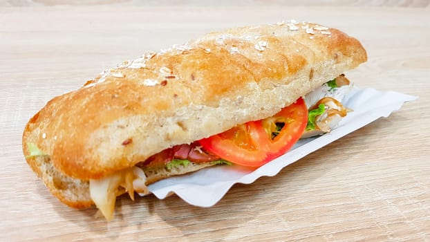 Ciabatta sandwich with lettuce, chicken and cheese on a wooden table.