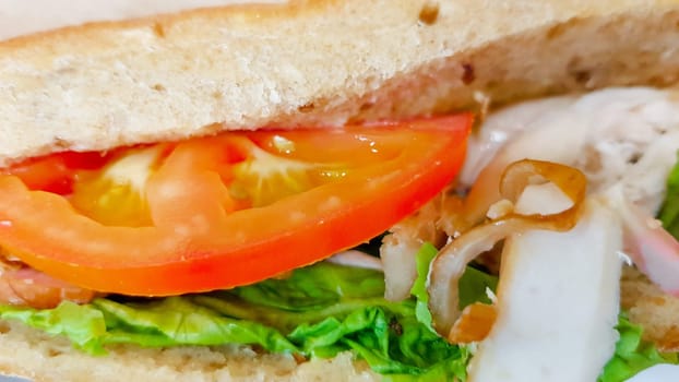 Ciabatta sandwich with lettuce, chicken and cheese on a wooden table.