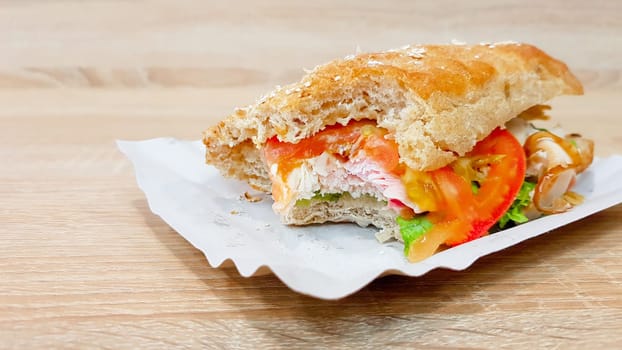 Ciabatta sandwich with lettuce, chicken and cheese on a wooden table.