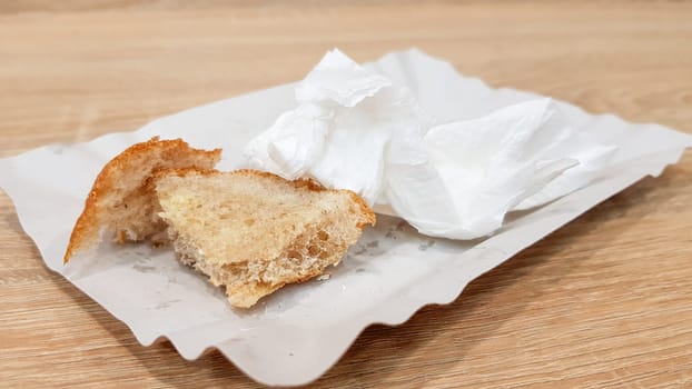 Leftover food on a paper plate and empty dirty paper coffee cup on a wooden table in a fast food cafe.