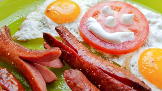 Top view of fried egg and sausages on a green plate, serving breakfast for the baby.