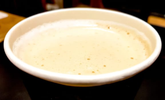Top view close-up of a paper cup of coffee with milk and foam on a dark background of cafe interior.