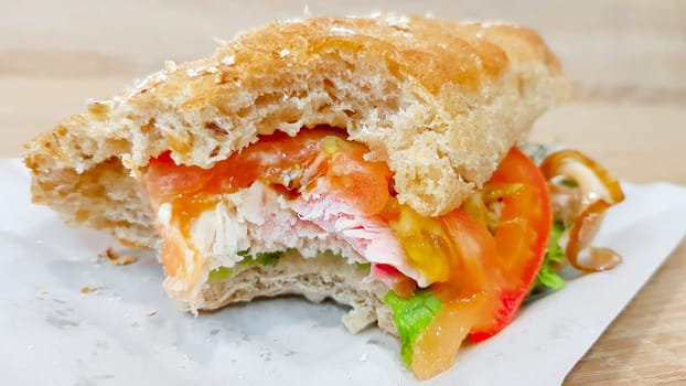 Ciabatta sandwich with lettuce, chicken and cheese on a wooden table.