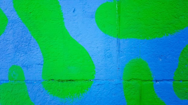 The concrete wall is painted in green and blue camouflage. Stains of paint on a stone wall, colorful background with copy space