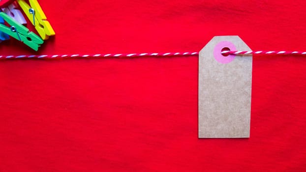 Colorful paper notes and clothespins on a red background. Empty color cardboard price tags, sale tag, gift tag, address label, luggage label hanging on clothes. Wooden clips. Layout, copy space for text, top view.