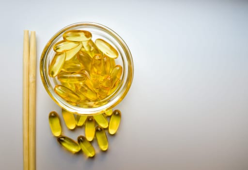 Fish oil capsules on a saucer with chopsticks. Bunch of vitamin omega 3 pills on a white background. Close-up, top view, high resolution product. Metabolism in the body. Body calcium