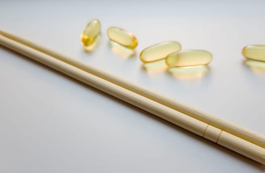 Fish oil capsules with Chinese chopsticks. Omega 3 on a white background. High Resolution Product. Food supplement. Vitamins for a healthy lifestyle. Fatty acid. Metabolism in the body