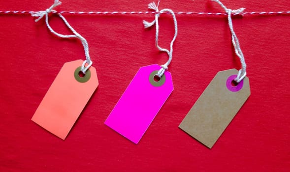 Three colored bright tags hang on a red rope on a red background. Copy space, place for text, flat lay