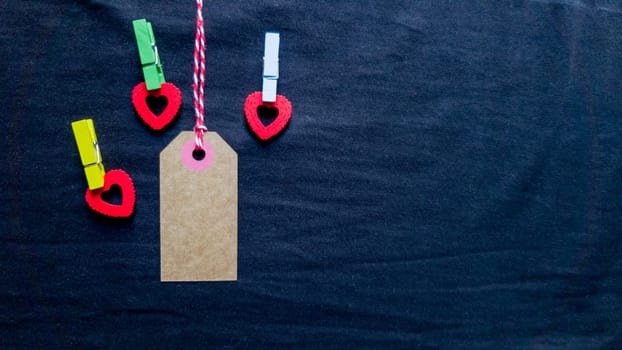 Natural blank old paper, fabric tag or label isolated on a dark background with a wooden red decorative heart. Holiday Valentine's Day, Black Friday, Christmas, New Year, birthday present for your beloved and beloved man or woman.