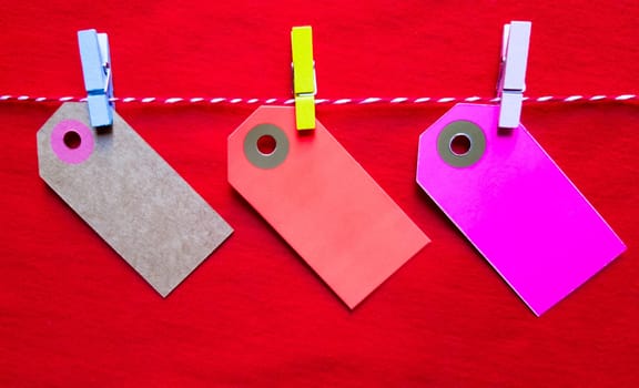 Colorful paper notes and clothespins on a red background. Empty color cardboard price tags, sale tag, gift tag, address label, luggage label hanging on clothes. Wooden clips. Layout, copy space for text, top view.