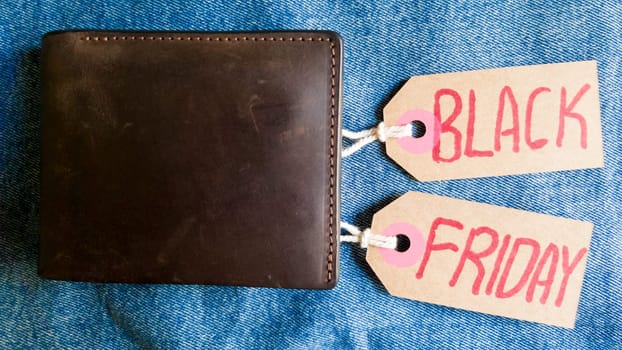 Brown wallet with money, dollars on a blue background, jeans texture, cardboard tag with red text Black Friday. Black Friday - International day of purchases, promotions, discounts, sales. Copy space, place for text, flat lay.