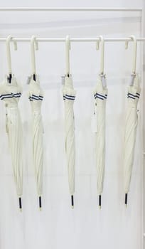 Five beige umbrellas hang on a coat hook hook, white background. Getting ready for the rainy season. Five modern umbrellas in a rack hanging in a white clothes hanger