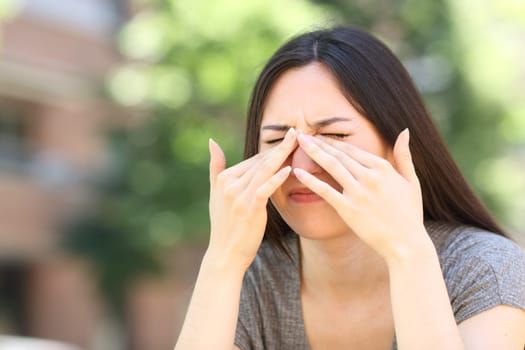 Asian woman scratching itchy eyes in the street