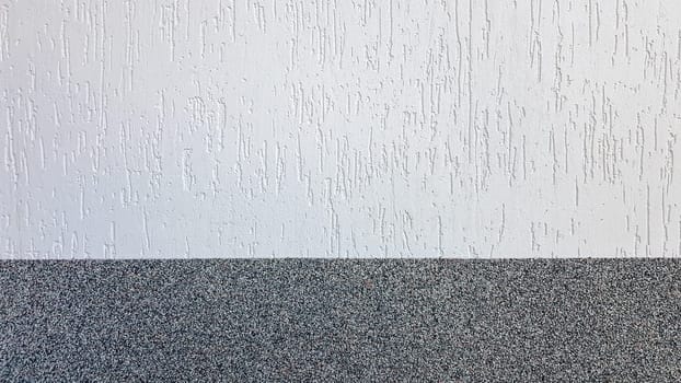 Gray marble chips and decorative light stucco on the wall divided by a horizontal line. Building facade background. Stucco texture on the street.