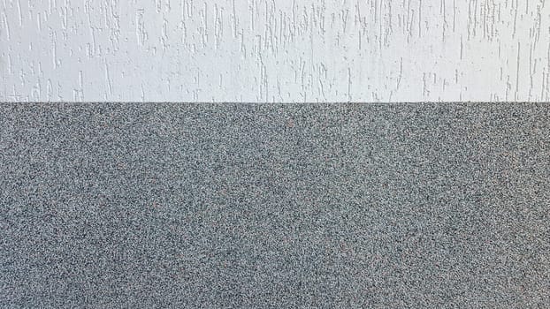 Gray marble chips and decorative light stucco on the wall divided by a horizontal line. Building facade background. Stucco texture on the street.