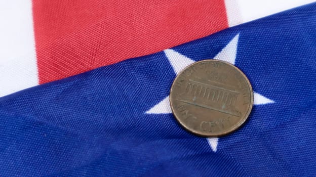 A 1 cent American dollar coin lies on the American flag. The currency is one cent over the flag of the United States