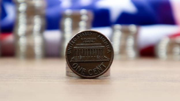 A 1 cent American dollar coin lies on the American flag. The currency is one cent over the flag of the United States