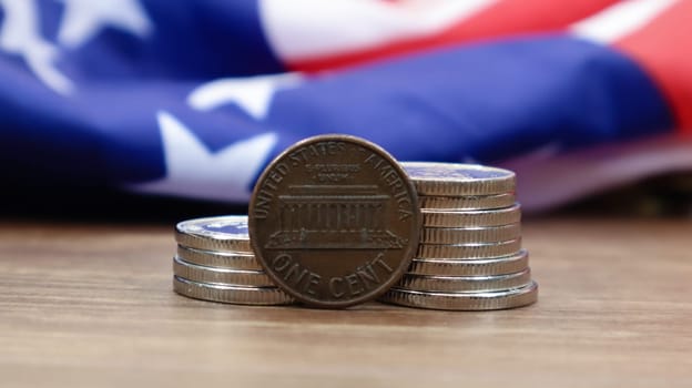 A 1 cent American dollar coin lies on the American flag. The currency is one cent over the flag of the United States