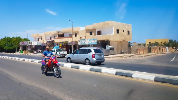 Egypt, Dahab - June 20, 2019: an Arab riding a scooter along one of the streets of Dahab. Desert Street. Egyptian residential buildings. The city of Dahab