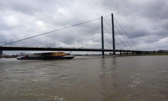 Germany, Dusseldorf - February 20, 2020: A loaded vessel in containers floats along the Rhine and under the Oberkassel bridge in the center of Dusseldorf. The ship goes against mating in the city.