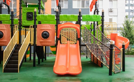A courtyard of high-rise buildings with a new modern colorful and large playground on a rainy summer day without people. Empty outdoor playground. A place for children's games and sports