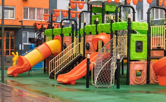 A courtyard of high-rise buildings with a new modern colorful and large playground on a rainy summer day without people. Empty outdoor playground. A place for children's games and sports