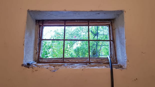 A rectangular basement window is tightened with a metal mesh and a grill. Technical window in the wall of an old gray building