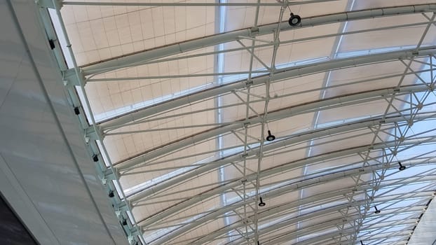 Curved roof with windows of a large shopping center indoors. Modern metal and glass ceiling construction